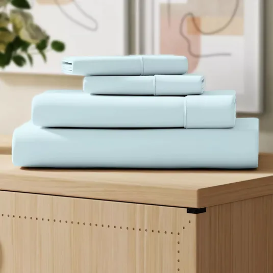 A neatly folded set of light blue bedsheets, placed on a wooden surface, with abstract art in the background.