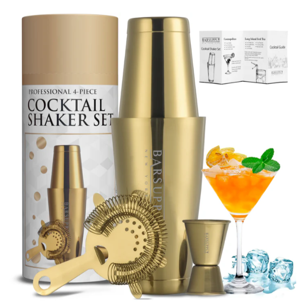 4-piece gold cocktail shaker set with shaker, strainer, jigger, and a recipe guide. Decorated with an orange cocktail garnish and ice cubes.