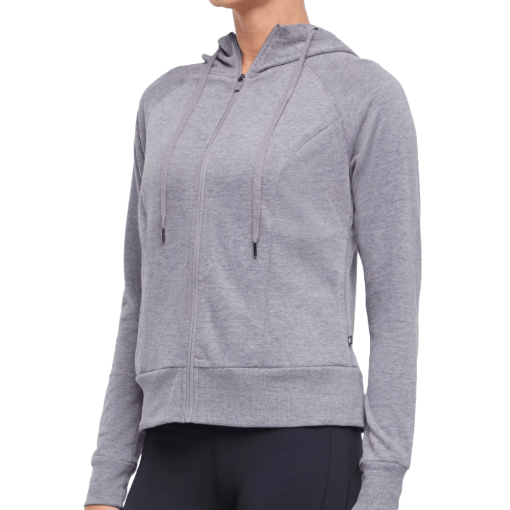 A person is wearing a grey zip-up hoodie with a hood and drawstrings, paired with dark leggings.