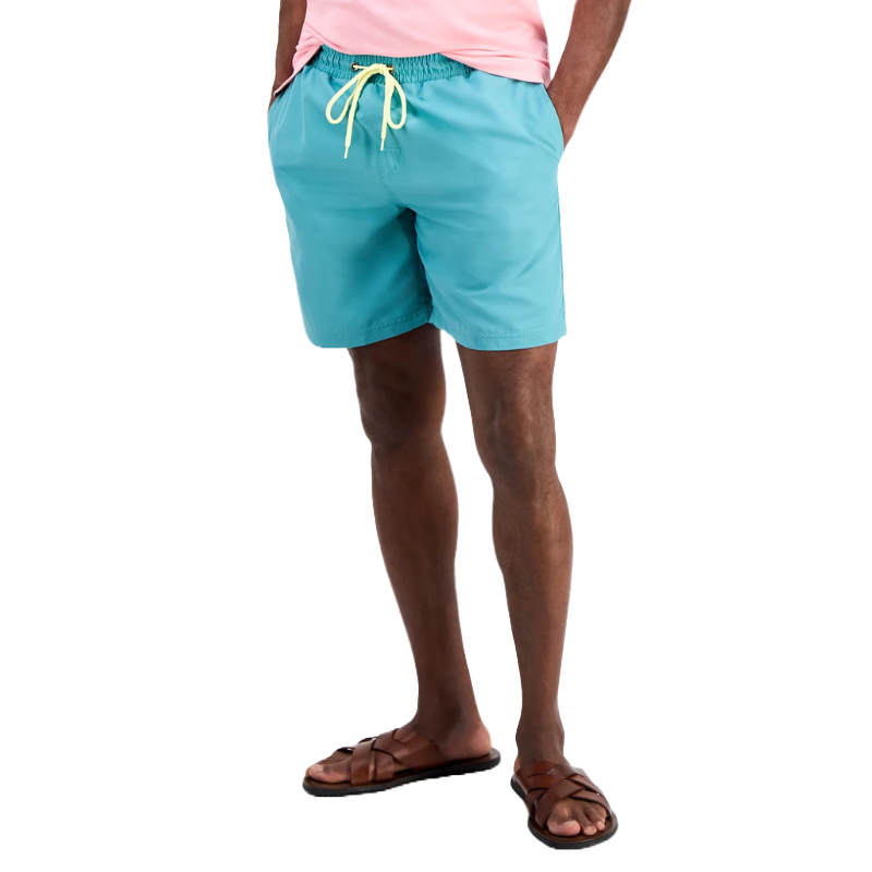 Man wearing light blue swim trunks with a yellow drawstring, paired with a light pink shirt, and brown sandals.
