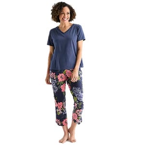 Woman wearing a blue V-neck T-shirt with floral-patterned pants featuring pink and purple flowers on a dark background.