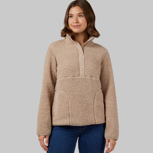 A woman wearing a beige fleece pullover with a half-zip front and a kangaroo pocket, paired with blue jeans.