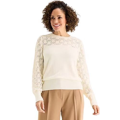 A woman wearing a white long-sleeve sweater with lace detail and beige pants.