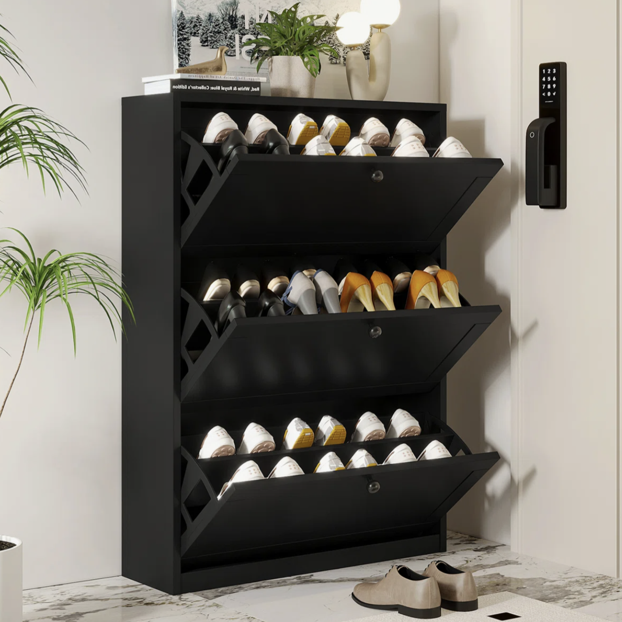 Black shoe cabinet with three pull-out drawers holding various pairs of shoes. It's placed in a room with plants and a digital lock on the wall.