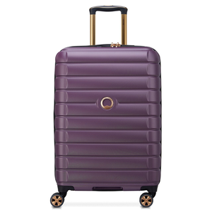 Purple Delsey upright spinner luggage with ribbed texture, telescoping handle, and four dual-spinner wheels. Features a gold accent around the handle and logo.