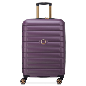 Purple Delsey upright spinner luggage with ribbed texture, telescoping handle, and four dual-spinner wheels. Features a gold accent around the handle and logo.