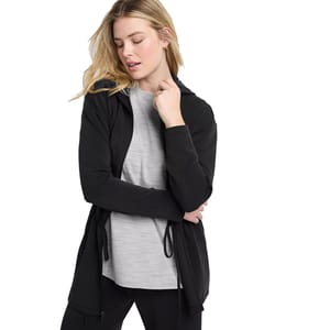 A woman is wearing a black zip-up hooded jacket over a light gray T-shirt with black pants.