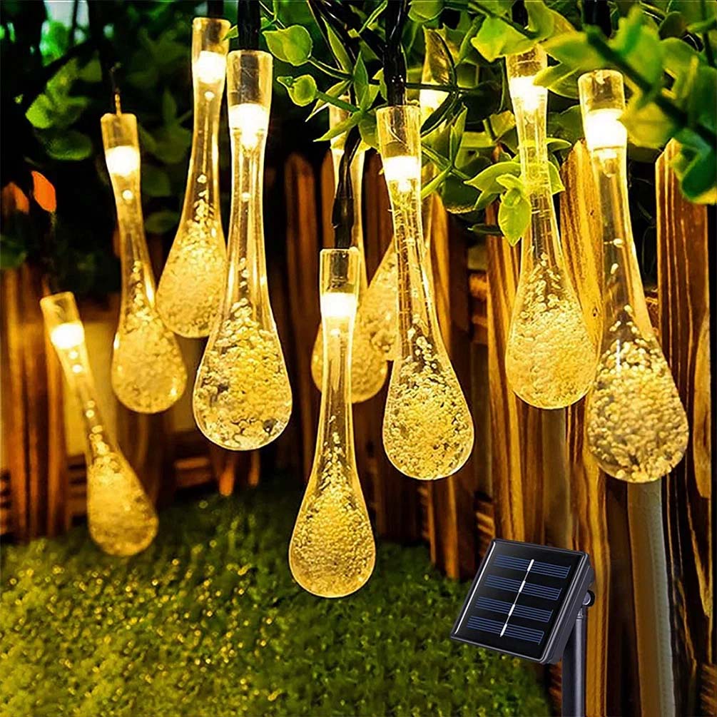 Hanging teardrop-shaped LED string lights with embedded bubbles, featuring a solar panel for outdoor use, strung along a wooden fence with greenery.
