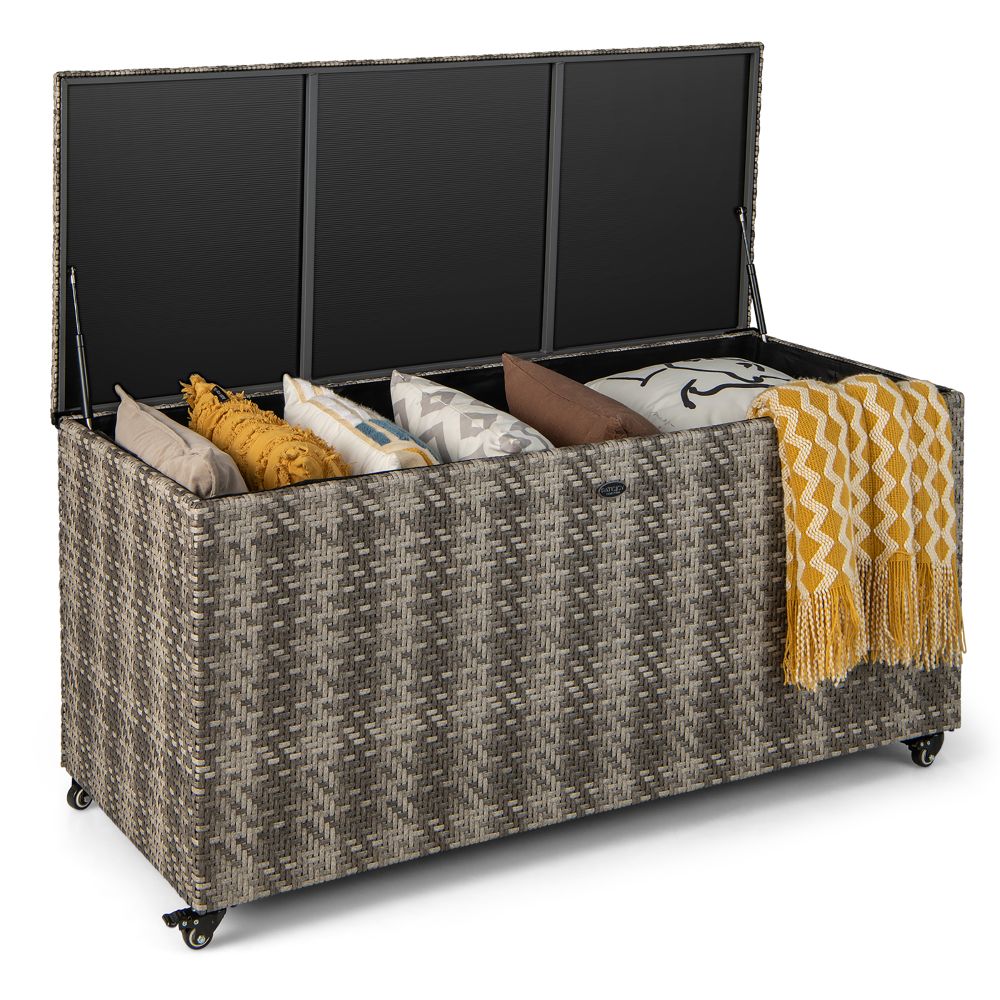 Wicker storage chest on wheels with an open lid, containing various pillows and a patterned yellow blanket.