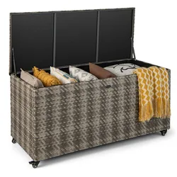 Wicker storage chest on wheels with an open lid, containing various pillows and a patterned yellow blanket.