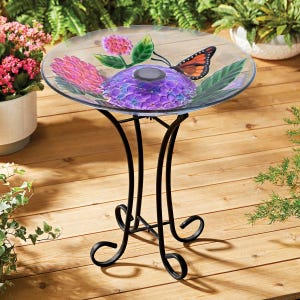 A glass side table featuring a colorful design with a purple flower and orange butterfly, supported by a black, decorative metal stand.