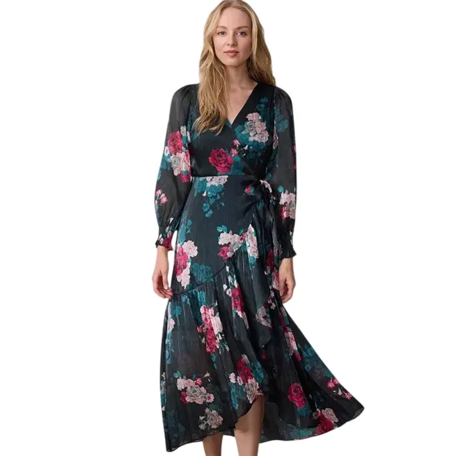A woman models a long-sleeved, wrap-style floral dress with a dark background and colorful flower patterns. She pairs it with ankle boots.