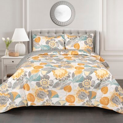 A queen-sized quilt set with a floral pattern in shades of orange, yellow, and gray, complemented by a polka dot pattern on the reverse side. The set includes two matching pillow shams.