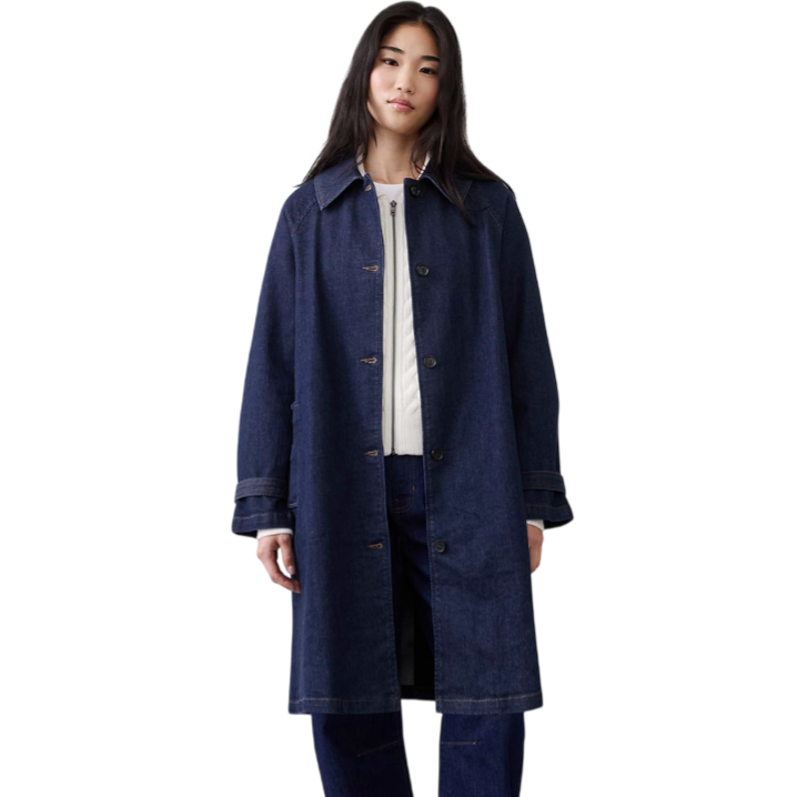 A person is wearing a long, dark denim coat over a white sweater, paired with matching denim pants and black loafers.