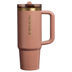 A rose-colored Stanley travel mug with a handle and a transparent lid featuring a straw opening.