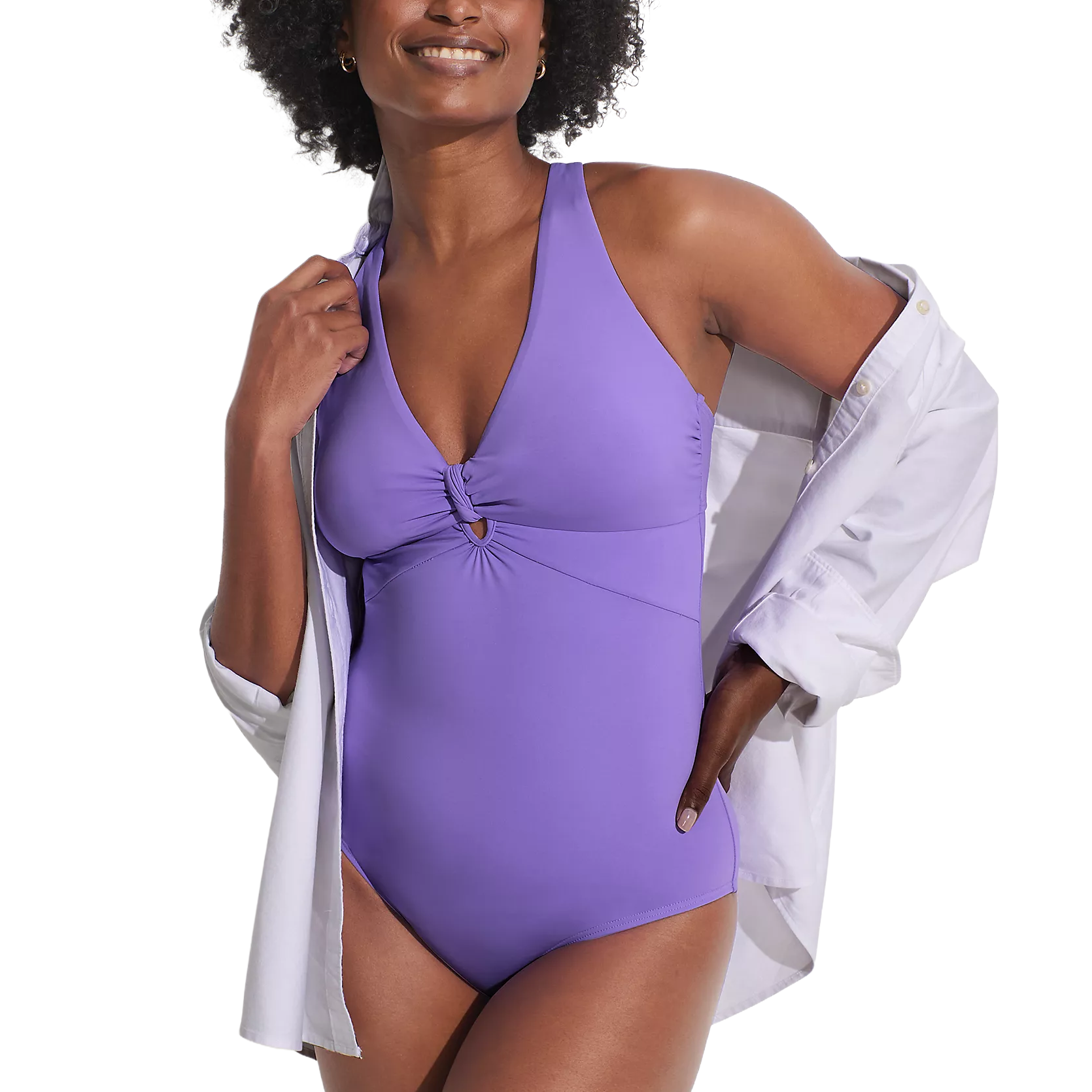 A woman is wearing a purple one-piece swimsuit with a knotted front detail and a white button-up shirt draped over her shoulders.