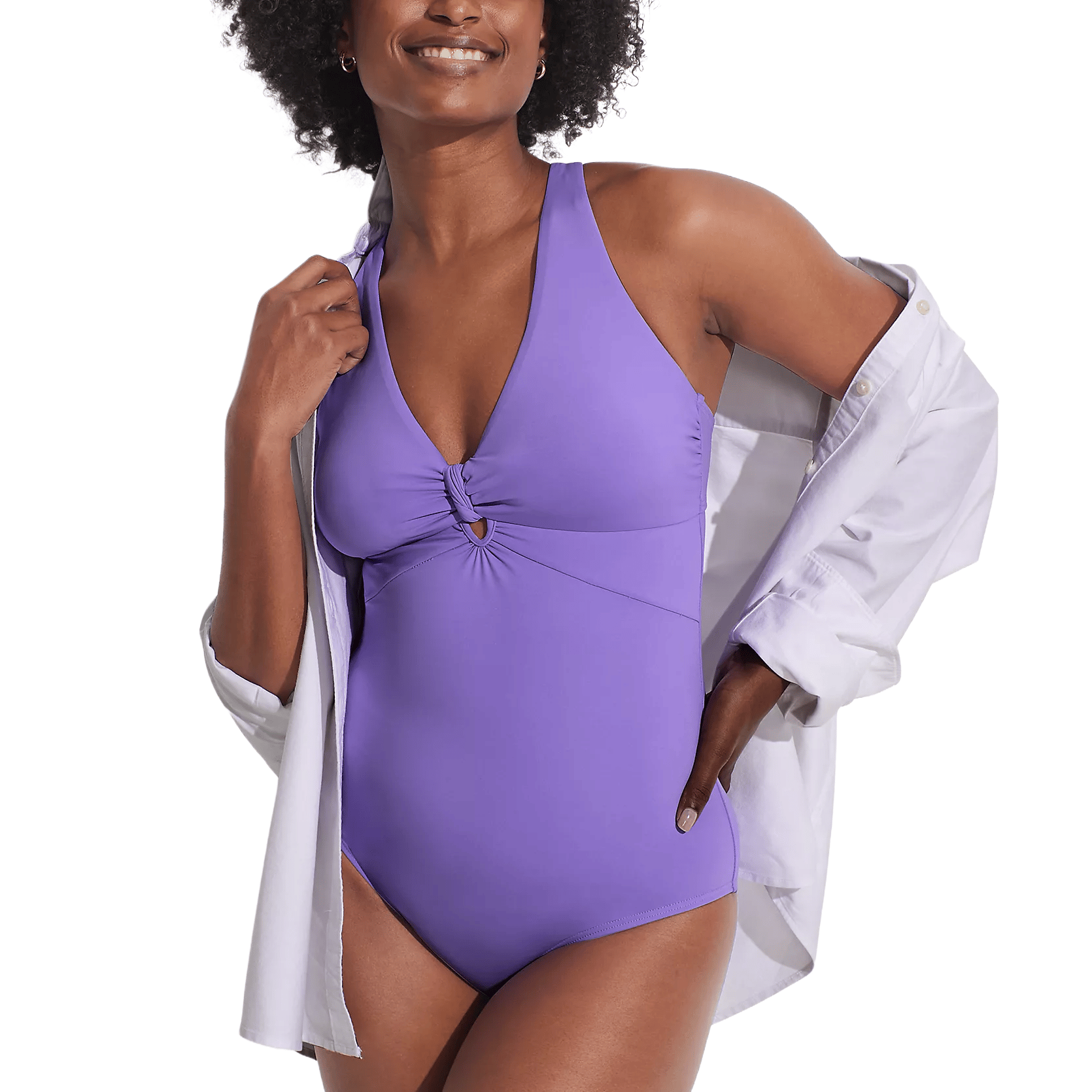 A woman is wearing a purple one-piece swimsuit with a knotted front detail and a white button-up shirt draped over her shoulders.