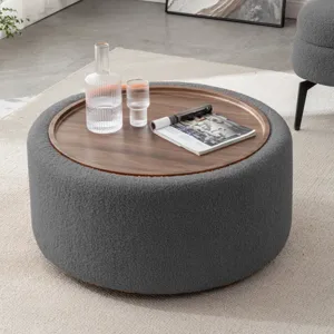 Round ottoman with a wooden tray top, holding a glass carafe, a tumbler, and a magazine. The setting is a modern living room with a white rug, and a gray chair is partially visible.