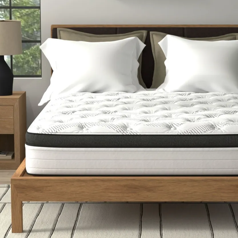 A neatly made bed with a white and black tufted mattress sits on a wooden platform, accompanied by two white pillows. The room includes a nightstand with a lamp, a potted plant, and a framed wall art piece.