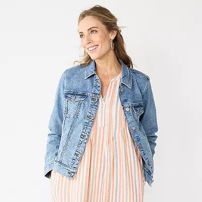 A woman is wearing a classic blue denim jacket with front chest pockets over a striped dress.