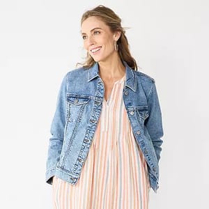 A woman is wearing a classic blue denim jacket with front chest pockets over a striped dress.