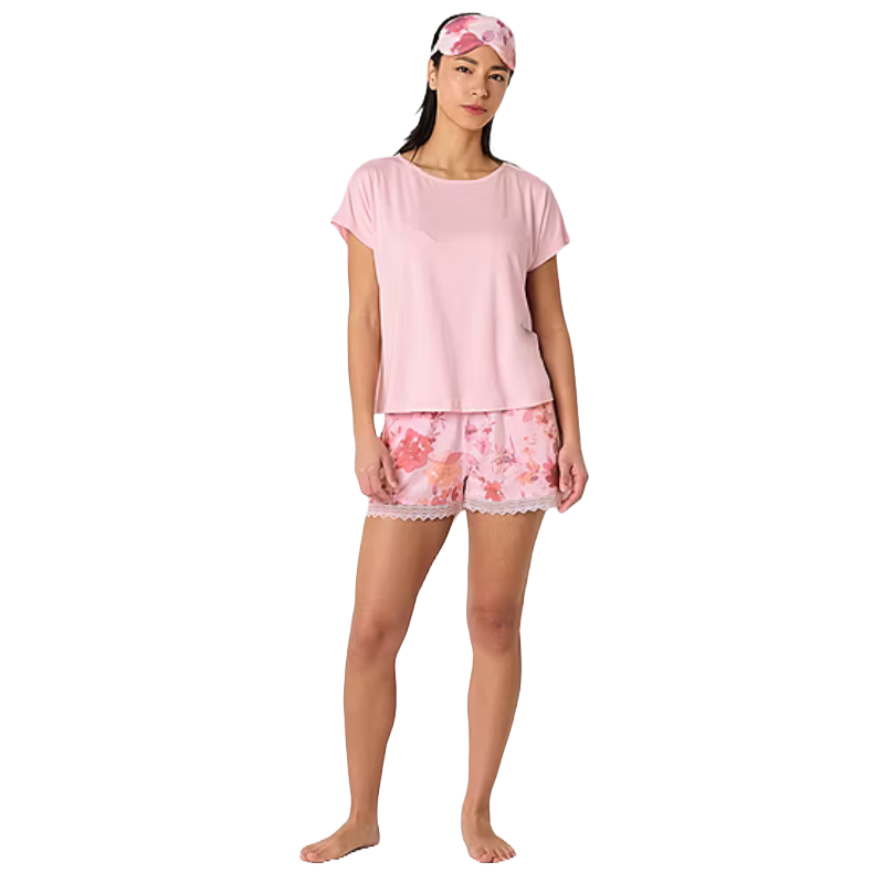 A person is wearing a pink sleepwear set that includes a short-sleeved top and floral shorts with lace trim, along with a matching floral sleep mask.