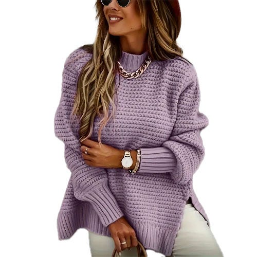 A person wearing a chunky knit lavender sweater, accessorized with a chain necklace and a wristwatch, paired with white pants.