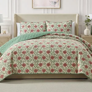 A beige bed with a floral-patterned quilt and shams featuring red flowers and green leaves, complemented by a light green quilted lining. Flanked by wooden nightstands with lamps and a decorative vase.