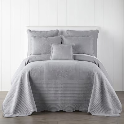Gray quilted bedding set with matching pillows on a bed against a white background.
