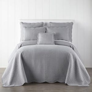 Gray quilted bedding set with matching pillows on a bed against a white background.