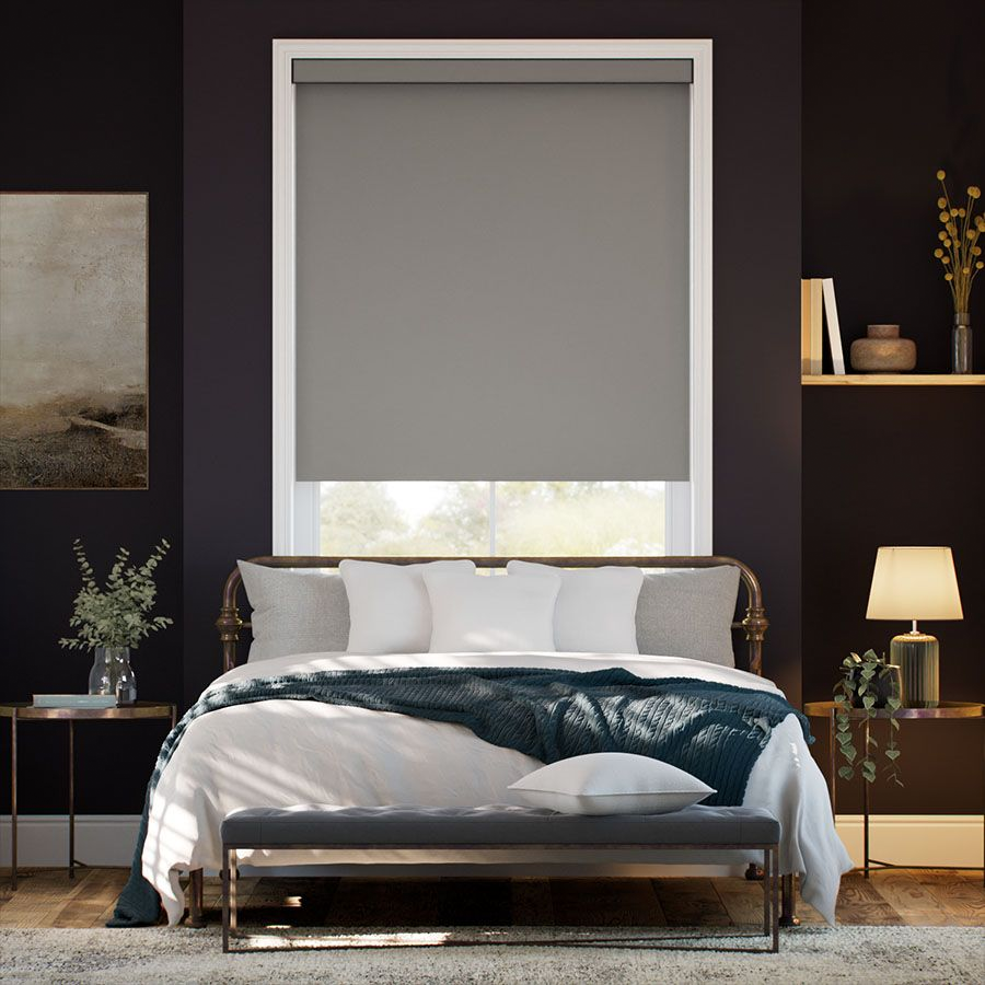 A bedroom features a bed with white and gray bedding, flanked by side tables with plants and a lamp. A gray roller blind covers the window, and shelves hold decorative items.