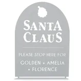 A decorative sign with \“Santa Claus\“ at the top and a request for Santa to stop for Golden, Amelia, and Florence. The sign has a cut-out design and a silhouette of Santa's head.