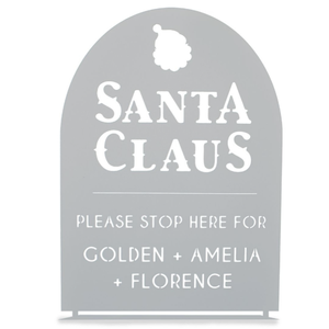 A decorative sign with \“Santa Claus\“ at the top and a request for Santa to stop for Golden, Amelia, and Florence. The sign has a cut-out design and a silhouette of Santa's head.