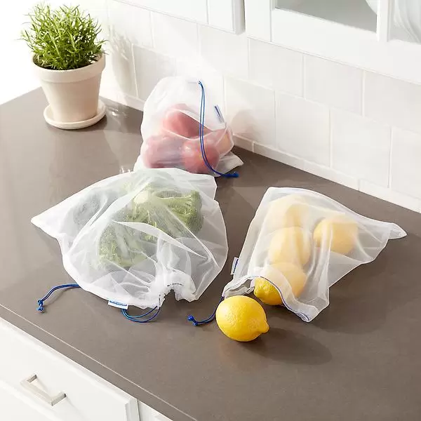 Reusable mesh produce bags with drawstrings, containing broccoli, lemons, and red bell peppers, are placed on a kitchen countertop.
