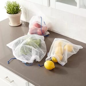 Reusable mesh produce bags with drawstrings, containing broccoli, lemons, and red bell peppers, are placed on a kitchen countertop.