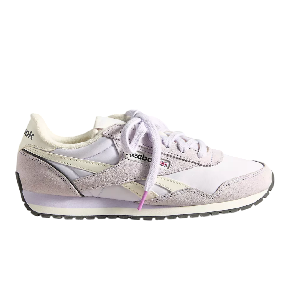 A lavender and white Reebok Classic shoe with suede and leather detailing, featuring a soft plush lining and a black and white rubber sole.