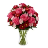 A bouquet featuring pink roses, pink carnations, and red chrysanthemums arranged in a clear glass vase.