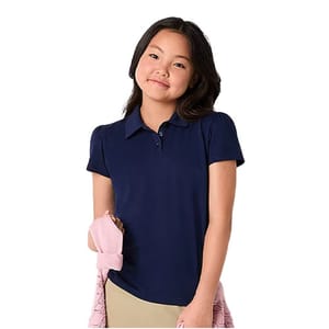 A young girl wearing a navy blue polo shirt stands holding a light pink jacket.