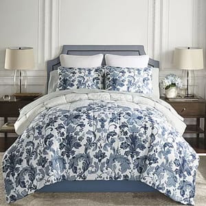 A bed features a blue and white floral comforter set with matching pillow shams, flanked by two wooden nightstands with lamps and decorative items.
