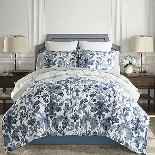 A bed features a blue and white floral comforter set with matching pillow shams, flanked by two wooden nightstands with lamps and decorative items.