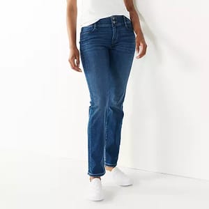 A person is wearing blue denim tummy-control jeans that have a slim fit and a mid-rise waist, paired with white sneakers.