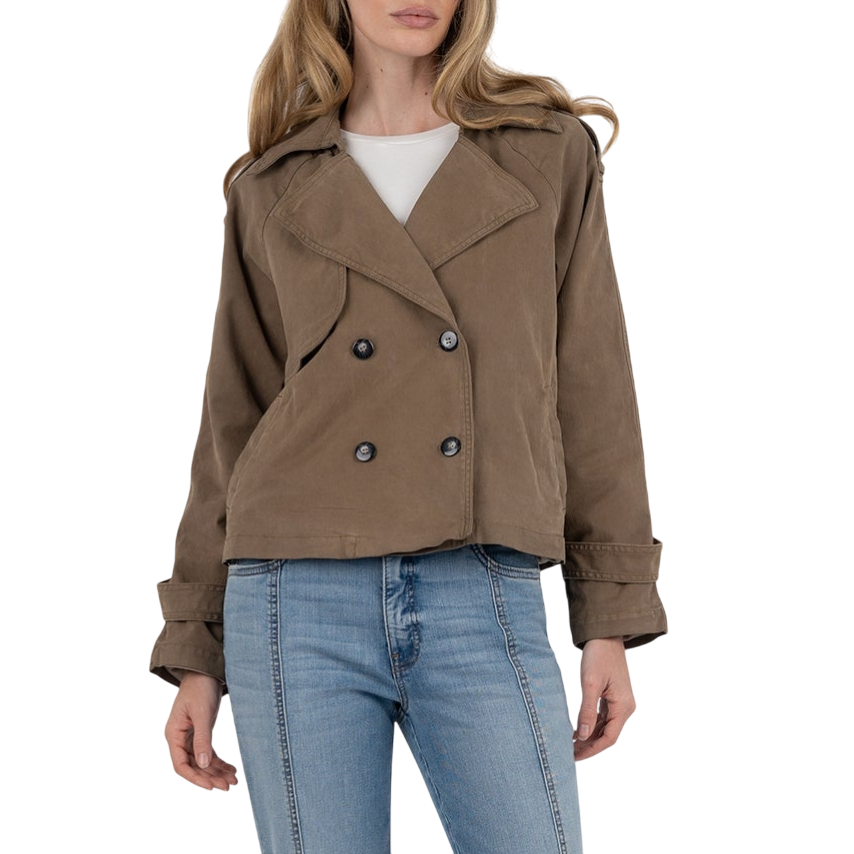 A woman is wearing a brown double-breasted jacket over a white shirt, paired with light blue flared jeans and black pointed-toe shoes.