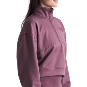 A woman is wearing a mauve, quarter-zip fleece pullover from The North Face, featuring a high collar and minimalistic design.
