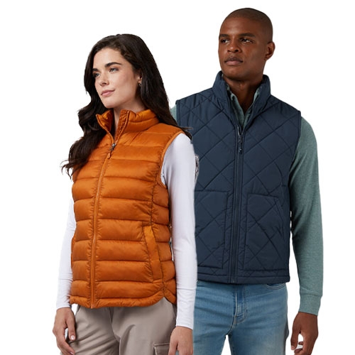 Two people wearing quilted vests; the woman wears an orange vest with a white long-sleeve top, and the man wears a navy vest with a green long-sleeve top and jeans.