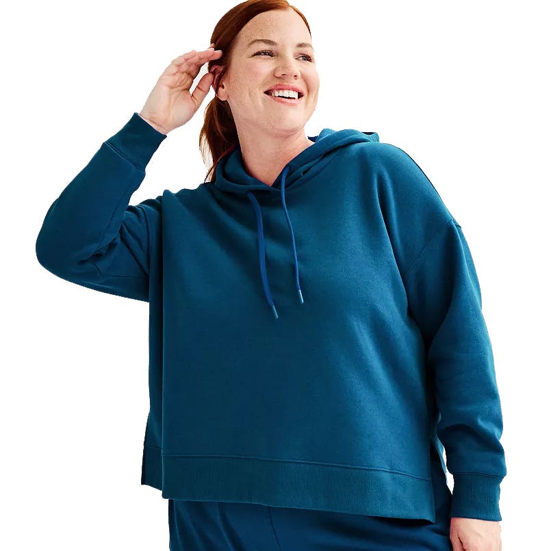 A person is wearing a teal hooded sweatshirt with a drawstring and matching pants, looking to the side and smiling.