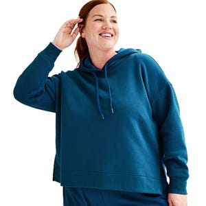 A person is wearing a teal hooded sweatshirt with a drawstring and matching pants, looking to the side and smiling.