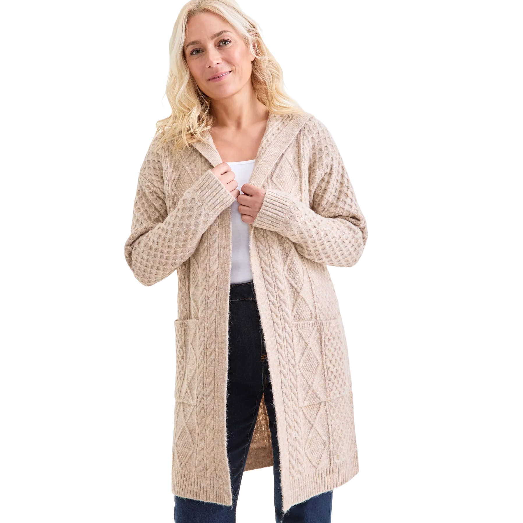 A woman is wearing a beige, hooded knit cardigan with a cable-knit pattern, two front pockets, and long sleeves, over a white top and dark jeans.