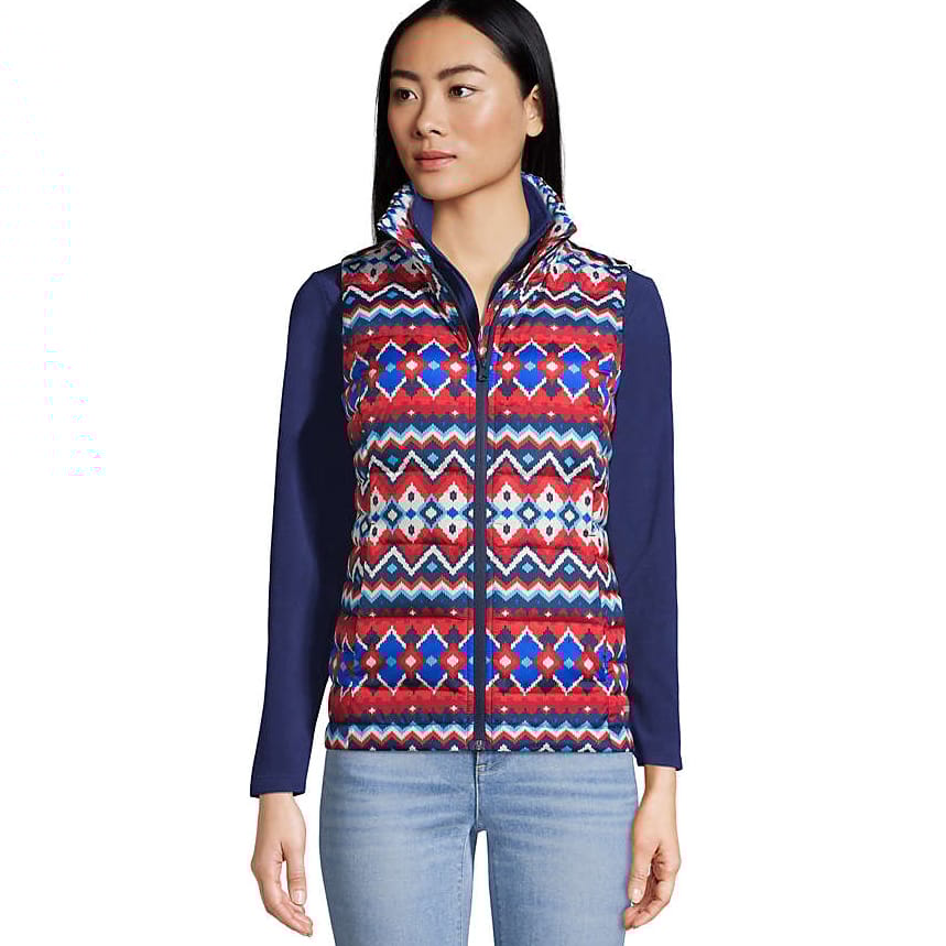 A woman is wearing a colorful, patterned zip-up vest over a navy long-sleeve shirt paired with light blue jeans.