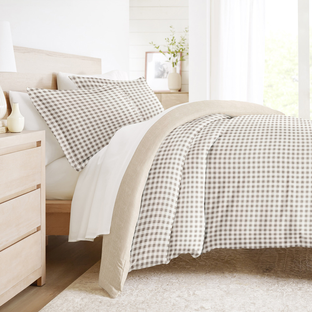 A cozy bedroom setup featuring a bed with a beige and white checkered duvet and pillows, complemented by a light wood nightstand and a neutral-colored, textured rug.
