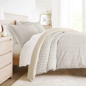 A cozy bedroom setup featuring a bed with a beige and white checkered duvet and pillows, complemented by a light wood nightstand and a neutral-colored, textured rug.
